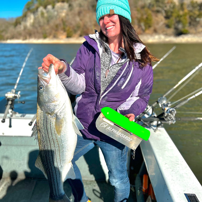 Person smiling while holding the green Alphaboardz planer board in their left hand and a fish in their right hand.